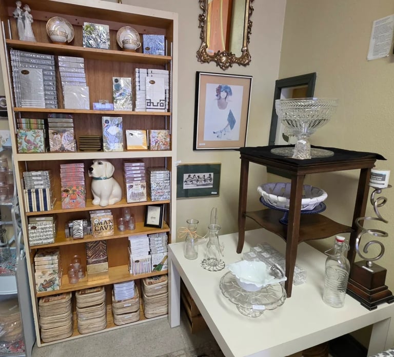 Interior home décor display with a wooden shelving unit, a side table with glassware, and framed artwork on the walls