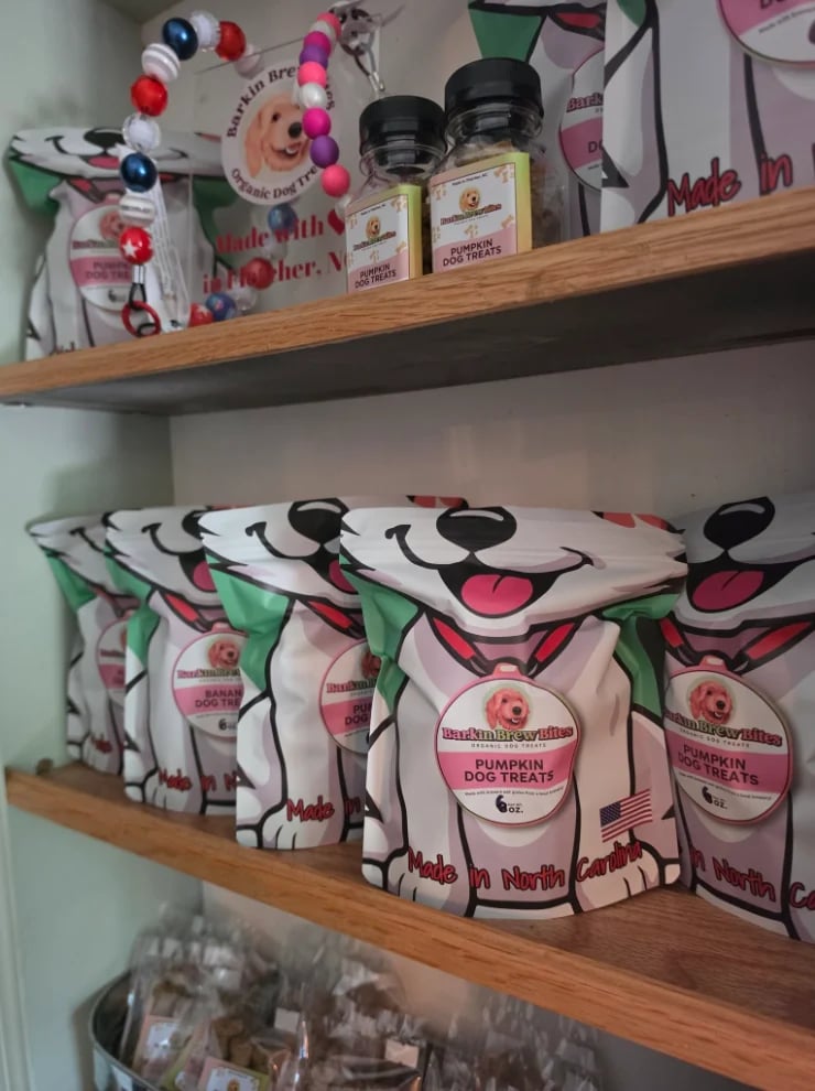 Wooden shelves displaying dog-themed treat packaging in pink and green designs with glass jars and a decorative pom-pom garland