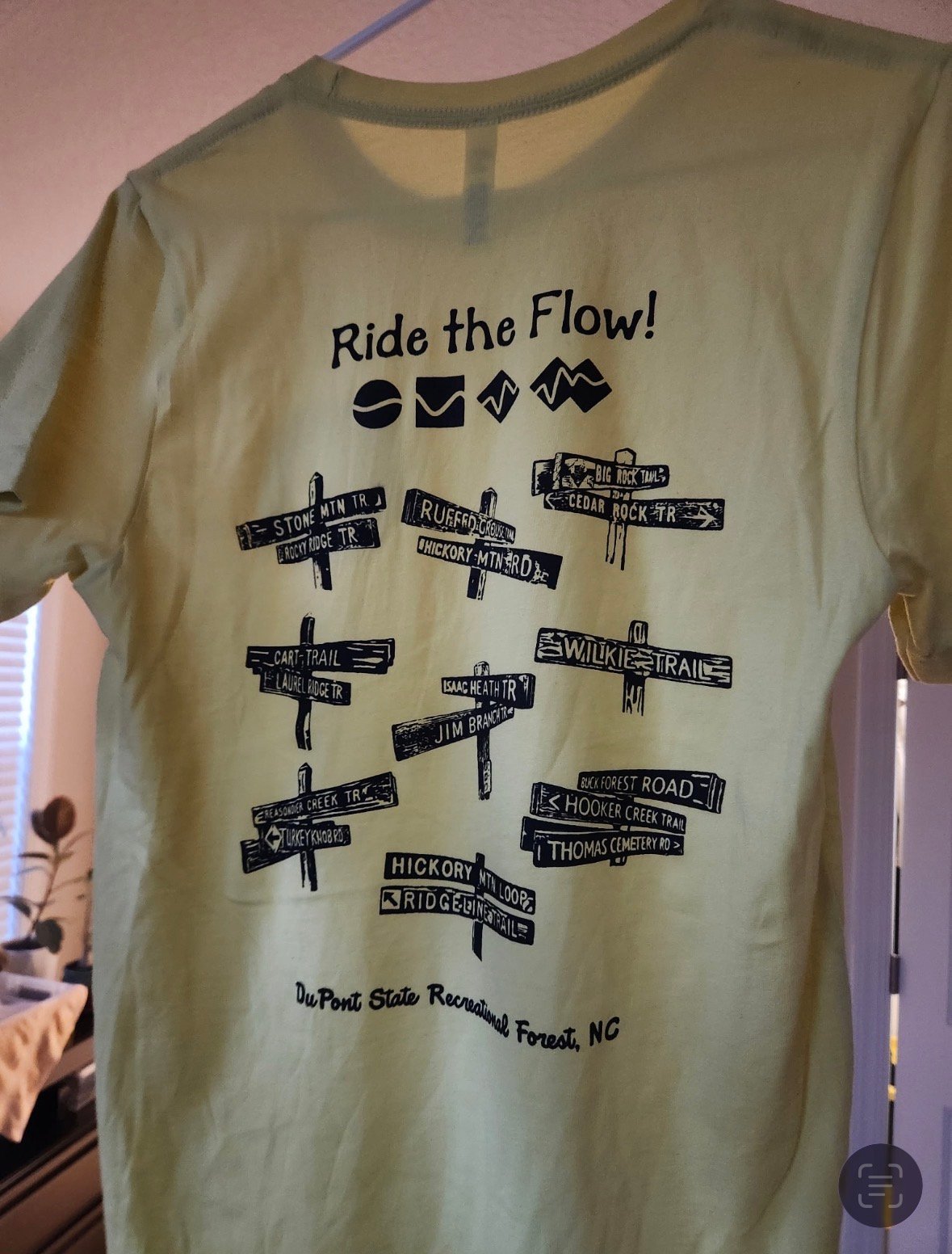 Tan t-shirt with Ride the Flow design featuring directional symbols and overlapping street signs graphic