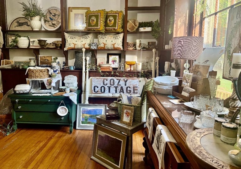 Cozy cottage interior with vintage decor, shelving units, green dresser, framed portraits, and eclectic home furnishings arranged throughout the room