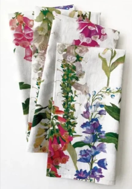 Stack of folded kitchen towels with colorful floral print patterns including pink, purple, and blue flowers on white background.