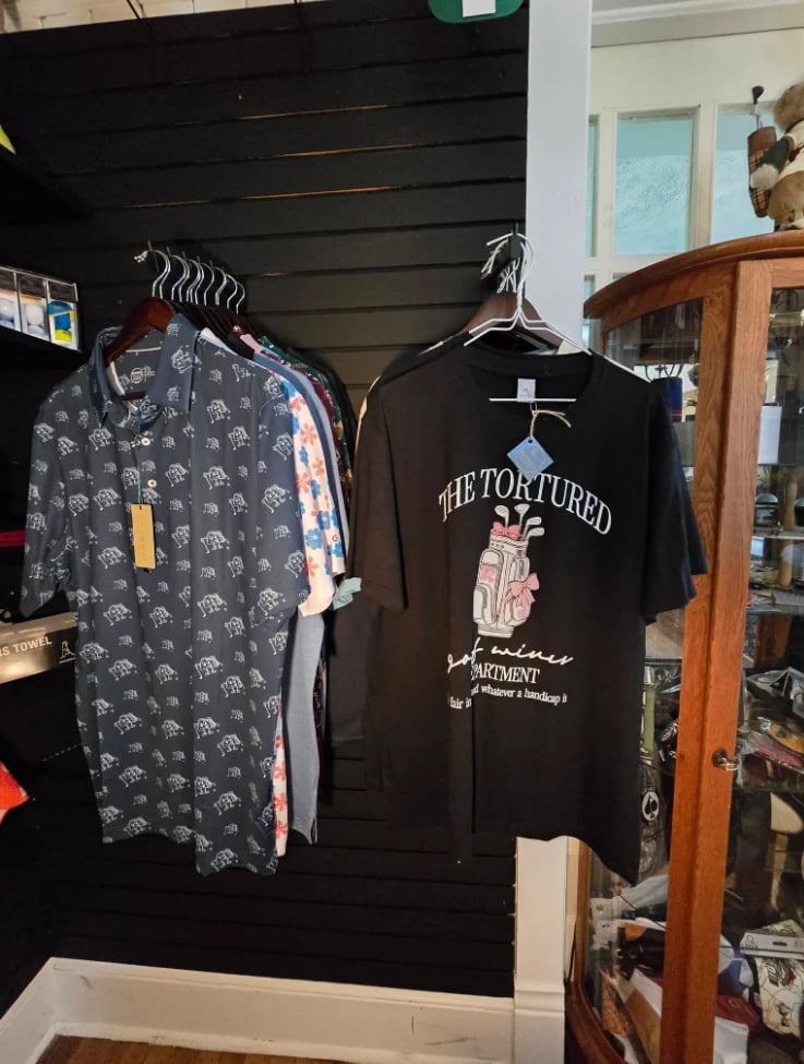 Two graphic t-shirts displayed on hangers against a black wall in a retail clothing store setting.