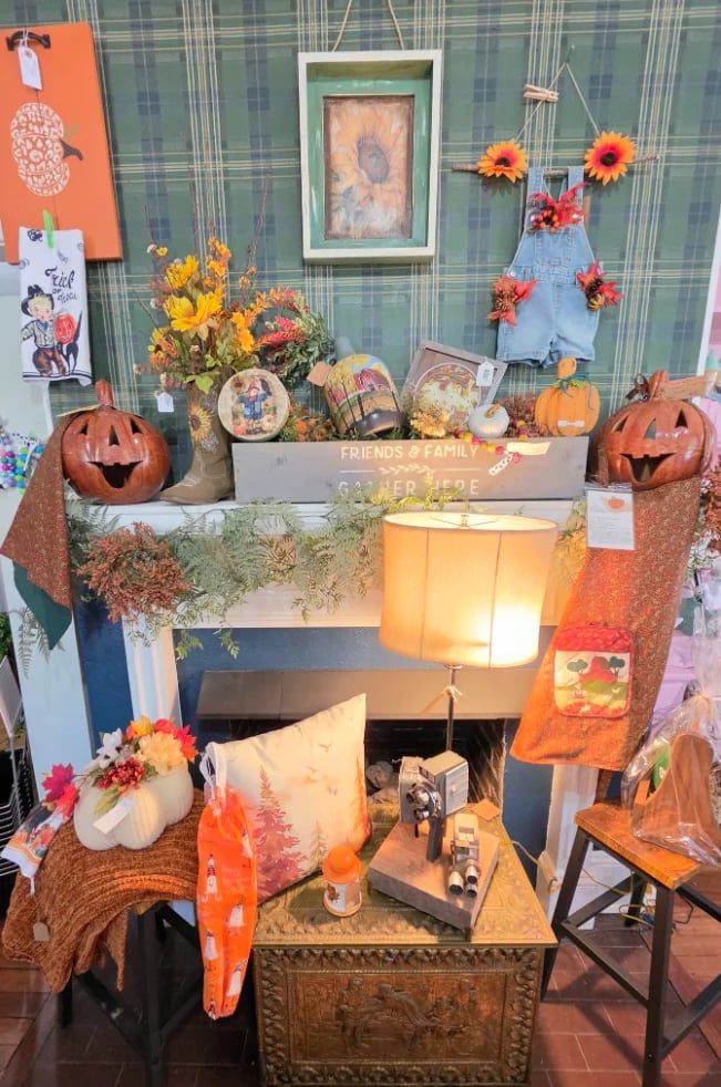 Seasonal fall display with carved pumpkins, autumn flowers, garland, and framed art arranged across shelving and a fireplace mantel