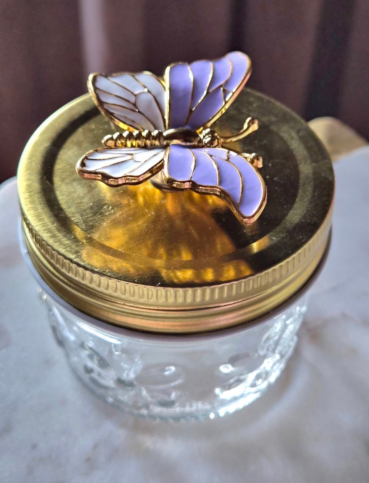 Decorative glass jar with gold lid topped by a blue and gold butterfly figurine