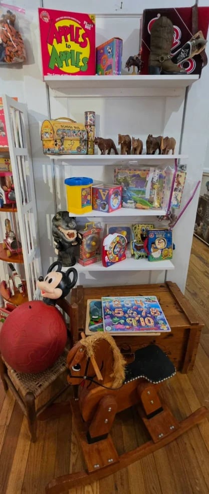 Vintage toy collection displayed on a white shelving unit with a wooden rocking horse and red ball in the foreground