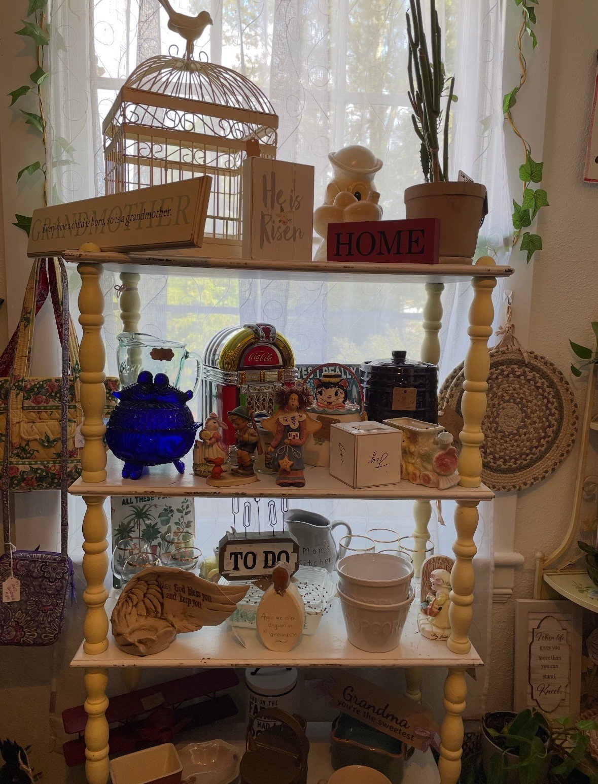 Wooden shelving unit displaying home decor items including a decorative birdcage, potted plants, candles, and wooden accents