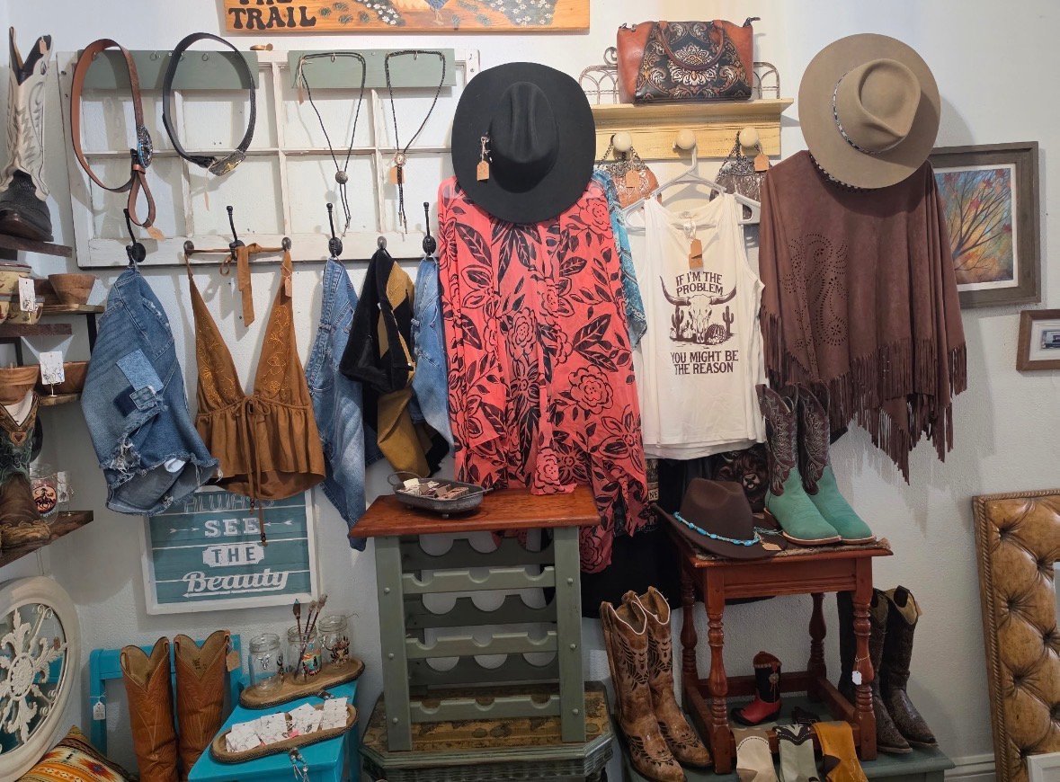 Rustic wall display with hanging clothing, hats, leather accessories, and western-themed decor items organized on shelves and hooks