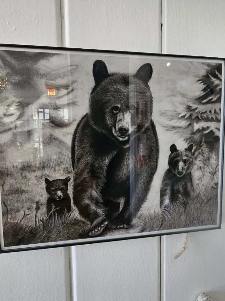 Framed black and white artwork depicting a mother bear with two cubs in a forest landscape with evergreen trees