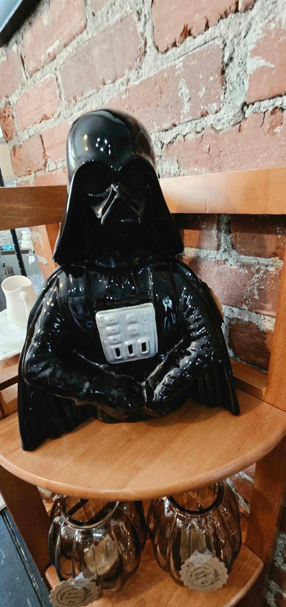Darth Vader figurine with electrical outlet on wooden shelf against brick wall background