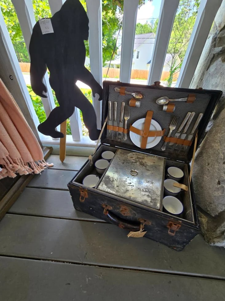 Vintage picnic basket with utensils and place settings displayed with Bigfoot cutout at window