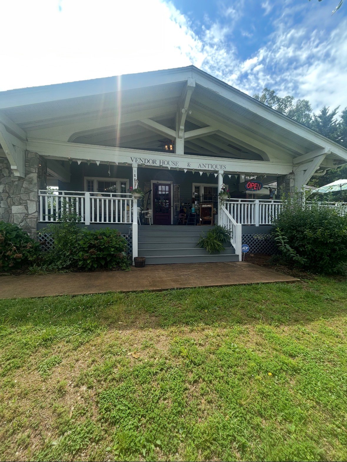 Vintage house antique shop with white porch, metal roof, and manicured lawn under blue sky