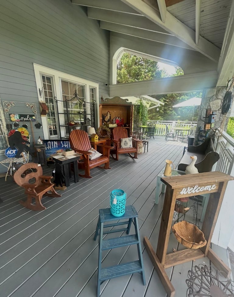 Covered porch with gray flooring, wood furniture, decorative items including a welcome sign, guitars, and scenic mountain views through open railings.