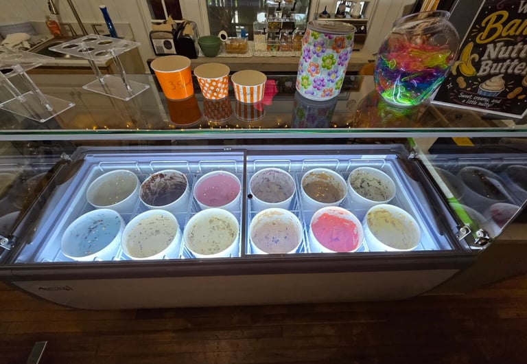 Ice cream display case with colorful frozen yogurt and ice cream flavors in white containers, with decorative cups on top of the counter