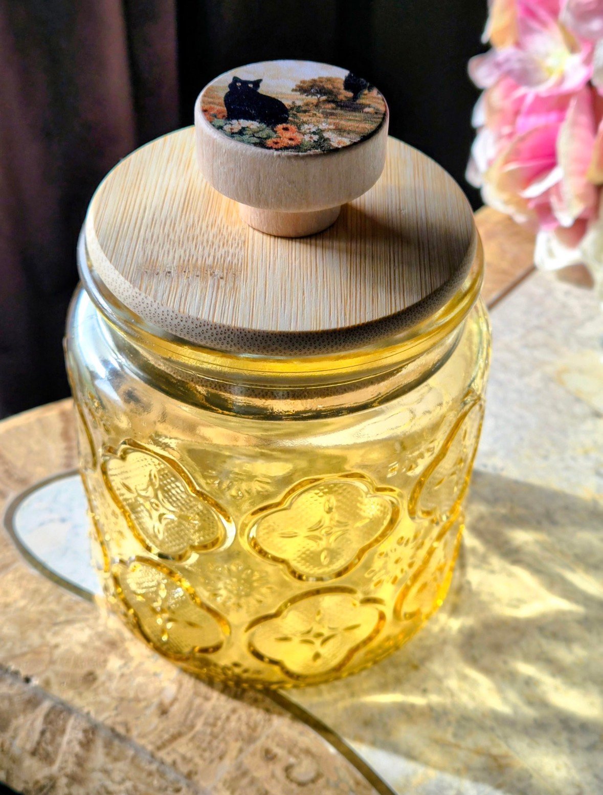 Glass jar with golden oil and embossed heart pattern, topped with wooden lid and decorative cork stopper with flowers