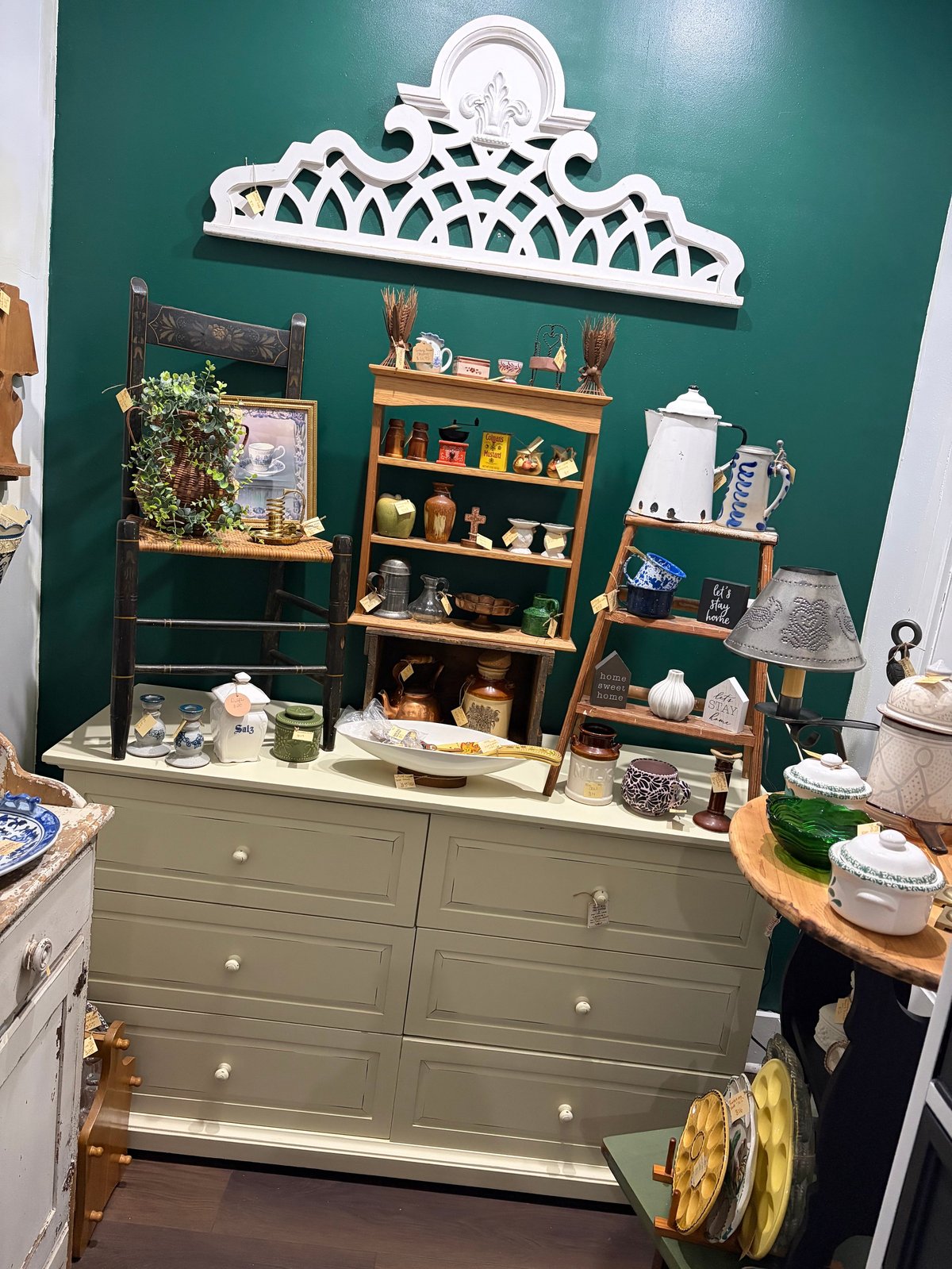 Kitchen display with green wall, wooden shelves holding decorative items, ornate white crown molding, and sage green cabinet base with kitchen accessories.