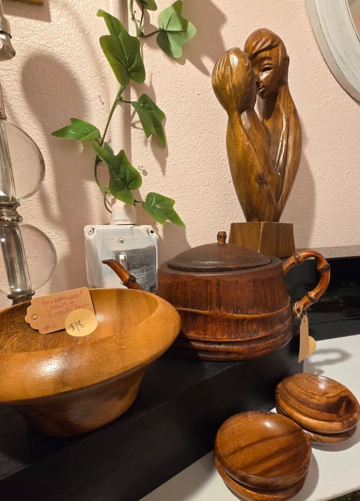 Wooden decorative items and bowls displayed on a shelf with a potted plant and carved wooden figurine