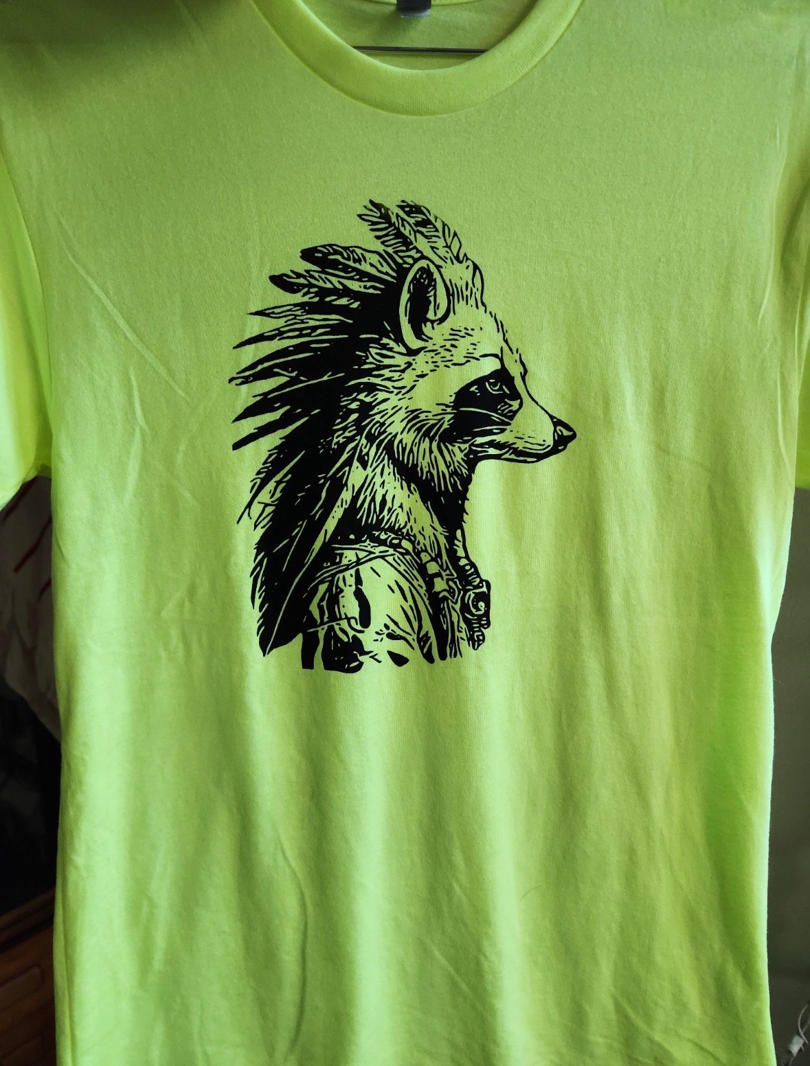Neon green t-shirt with black ink illustration of a wolf or fox head in profile with flowing mane and feathered details
