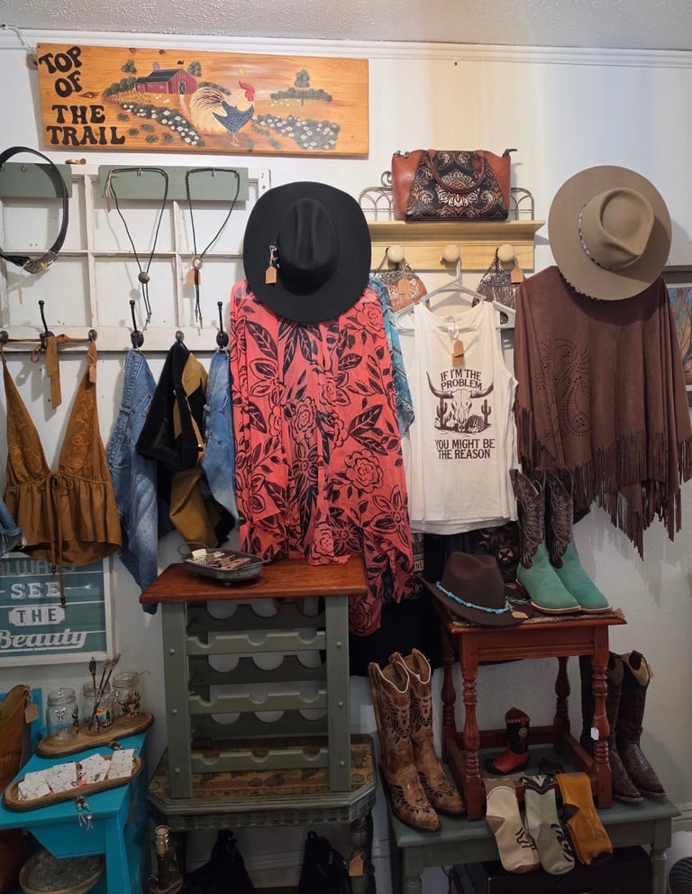 Western-themed retail display with mannequin wearing red and black patterned outfit and black hat, surrounded by cowboy boots, western apparel, hats, and rustic decor.