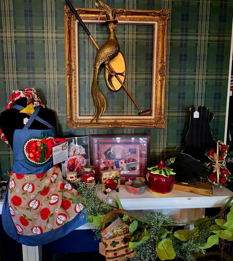 Display window featuring ornate gold frame with bird sculpture, vintage clothing, red florals, and decorative items against striped backdrop