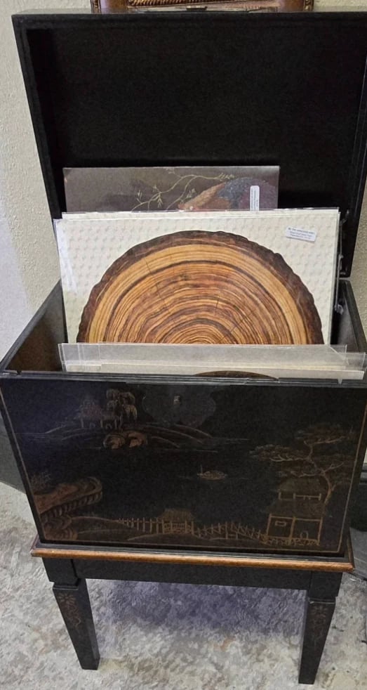 Open black wooden storage cabinet displaying tree ring cross-section artwork and nature photographs inside