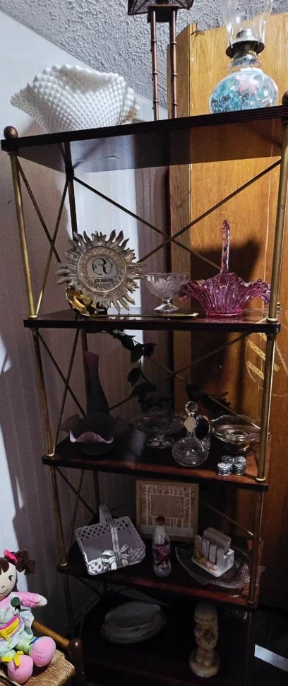 Black metal shelving unit displaying decorative items including ornamental plates, perfume bottles, and glassware against a wooden wall