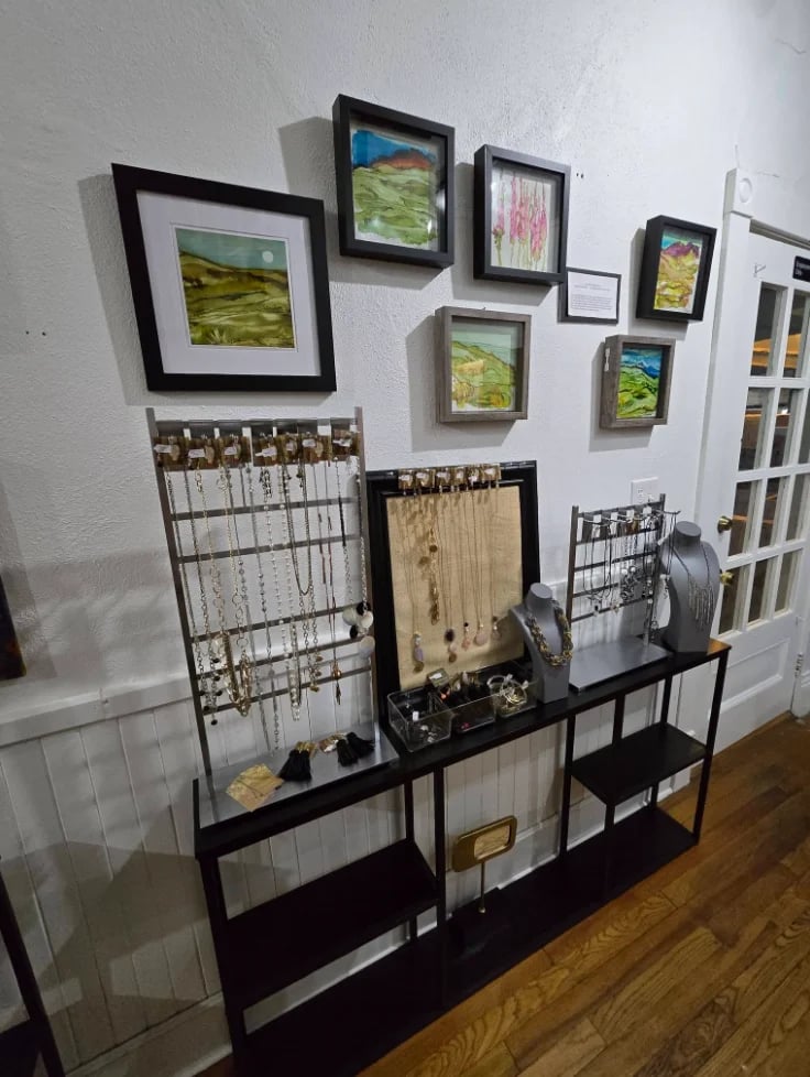 Gallery wall with framed landscape photos above black shelving unit displaying jewelry stands and merchandise on wooden floor