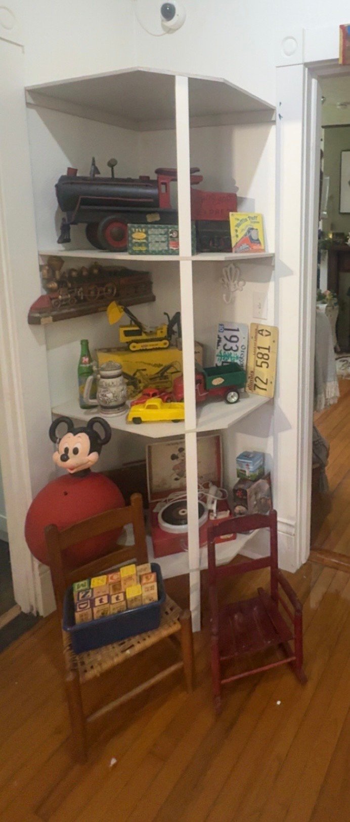 Corner display cabinet filled with vintage toys, collectibles, and memorabilia including toy trains, Mickey Mouse figure, and various decorative items on wooden shelves.