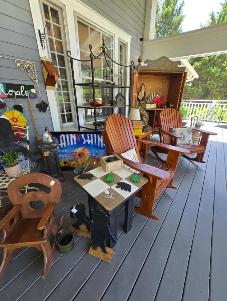 Outdoor deck with wooden furniture, including chairs and a small table, decorated with sunflowers and vintage items displayed for sale.