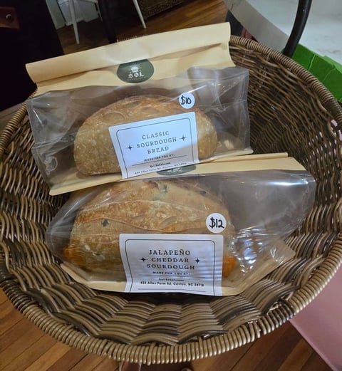 Two packaged sourdough breads in a woven basket, labeled Classic Sourdough Bread and Jalapeno Cheddar Sourdough from SOL Bakehouse