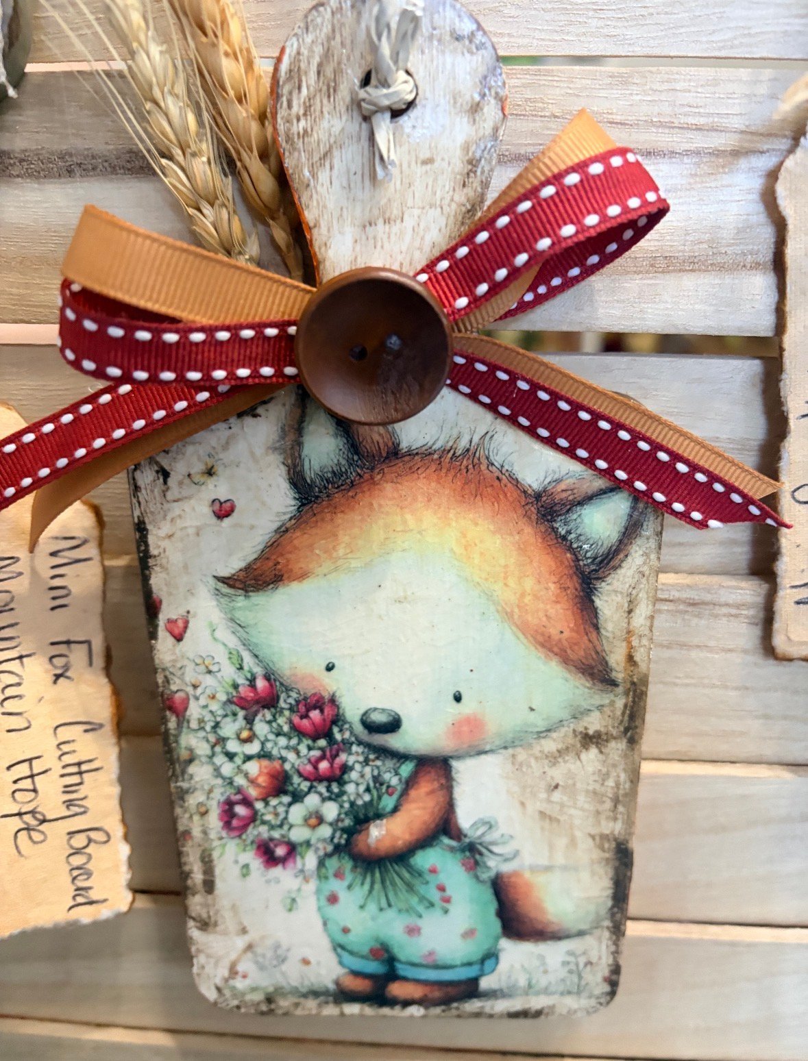 Wooden gift tag with whimsical fox illustration, red polka dot ribbon bow, and hanging string on whitewashed wood background