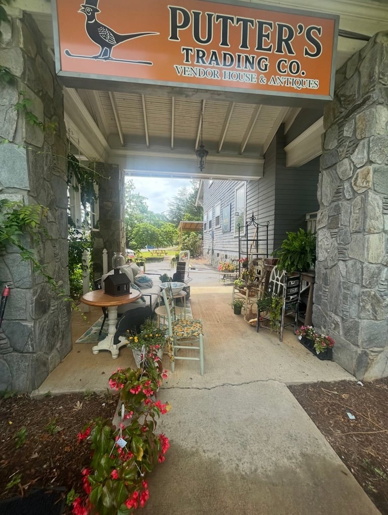 Putters Trading Co. vendor house storefront with stone archway, outdoor seating, potted plants, and signage visible from covered entrance