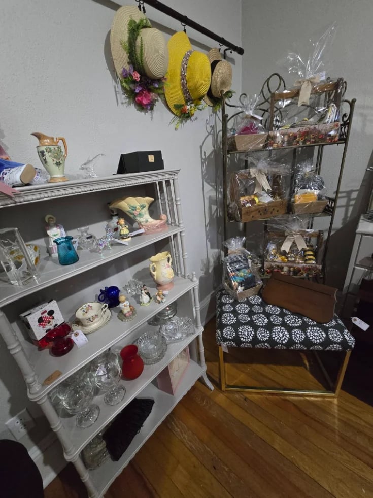 Interior room with glass display cabinets containing collectibles, decorative hats hanging from rod, and a metal shelving unit with various items on wooden flooring