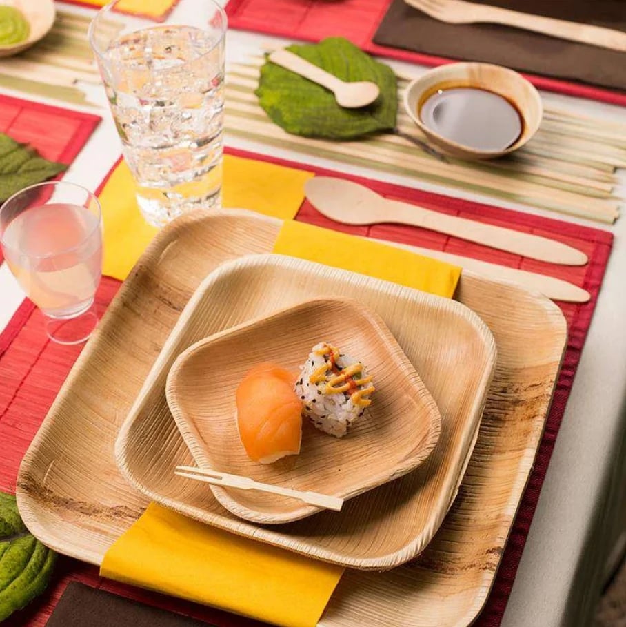 Asian dining setup with palm leaf plates containing nigiri sushi, drinks, and colorful red and yellow placemats