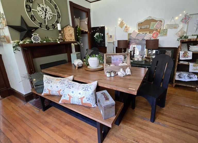Rustic dining room with wooden table, cushioned bench seat, black chairs, fireplace mantel with clock, and decorative wall items
