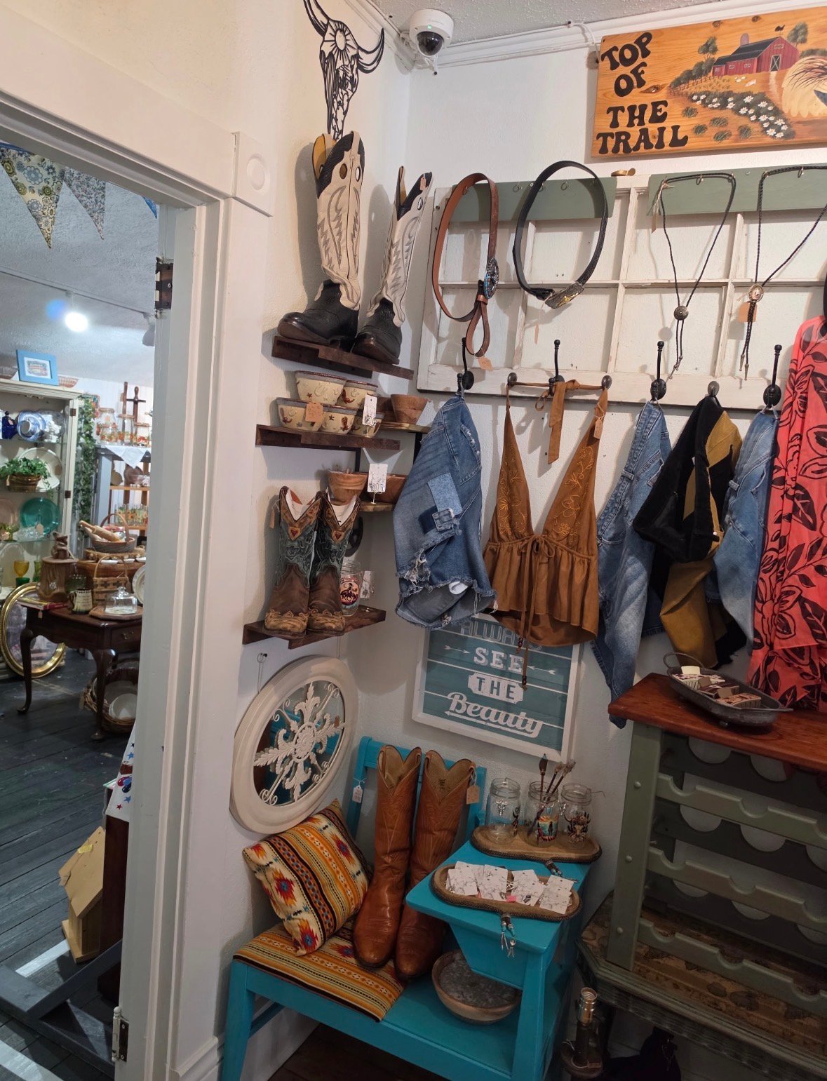 Western-themed wall display with hanging accessories including ropes, hats, scarves, boots, and decorative items on hooks and shelves
