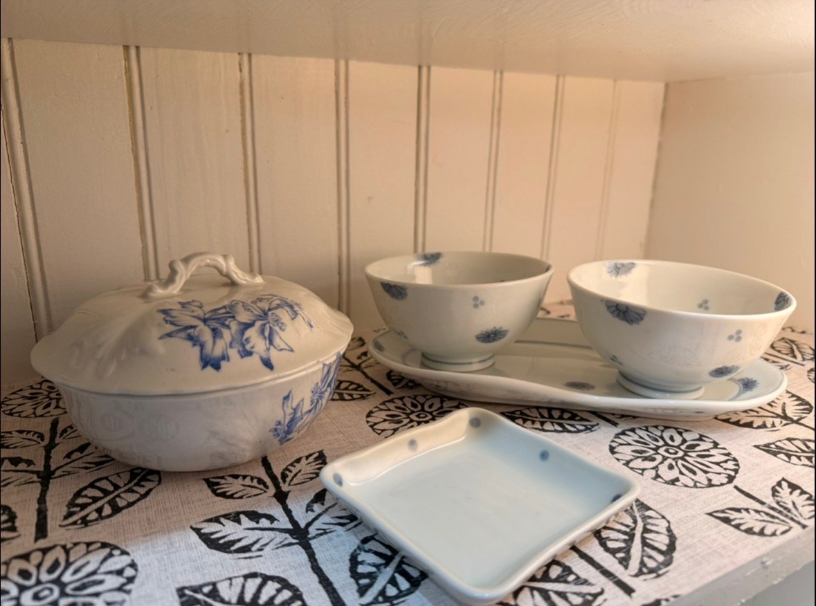 Collection of blue and white ceramic dishware including a covered tureen, bowls, and plates with floral and tree branch designs