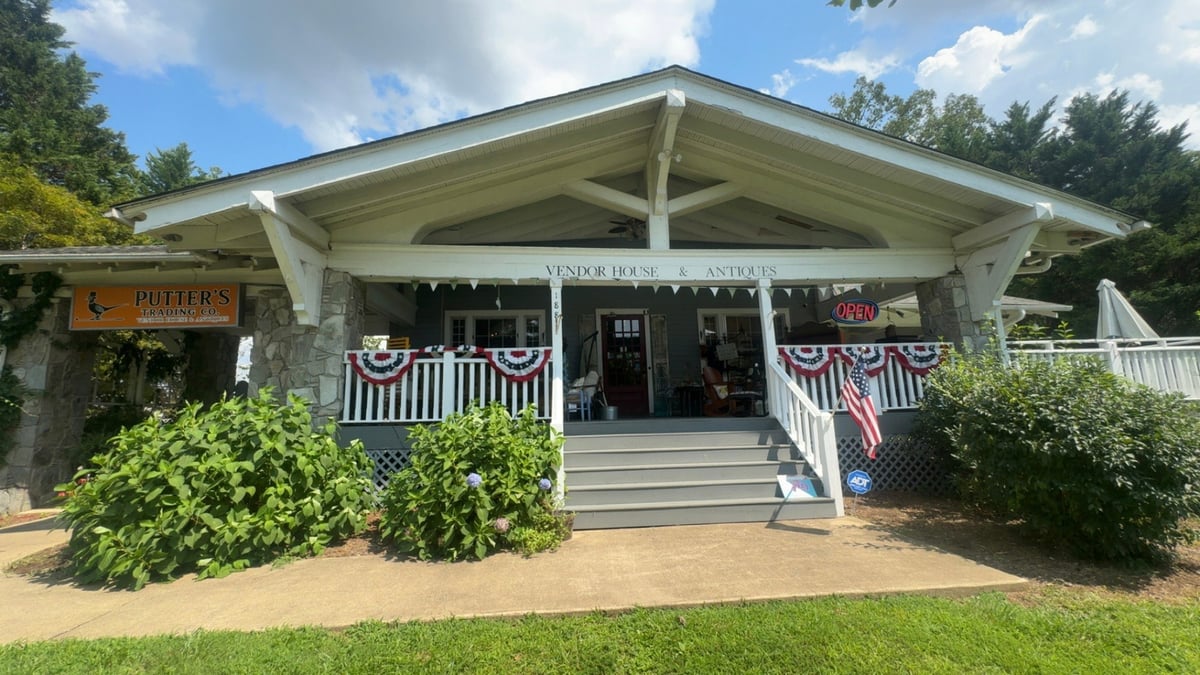 Charming white cottage-style building with American flag bunting and landscaping in a sunny outdoor setting